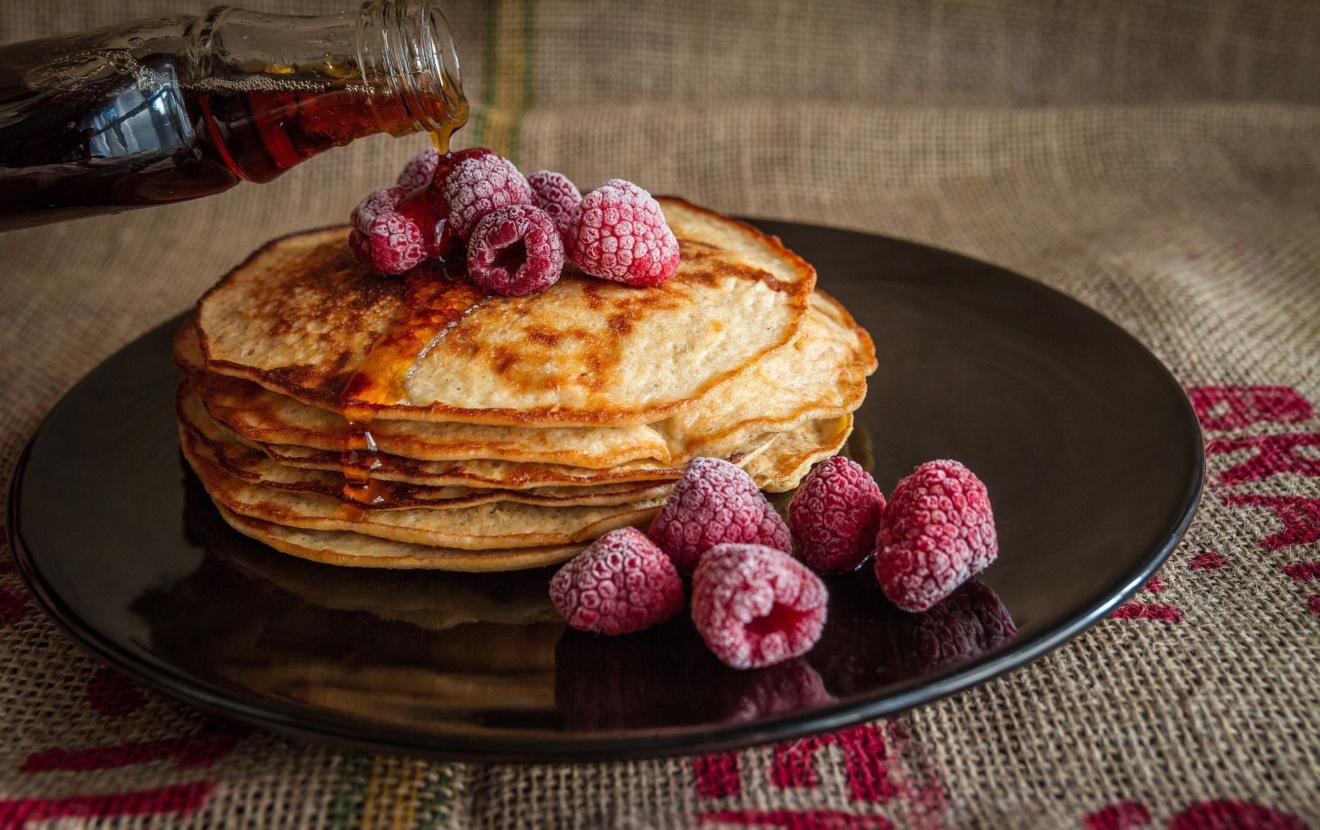 Una pila de tortitas con almíbar y frambuesas sobre un plato.