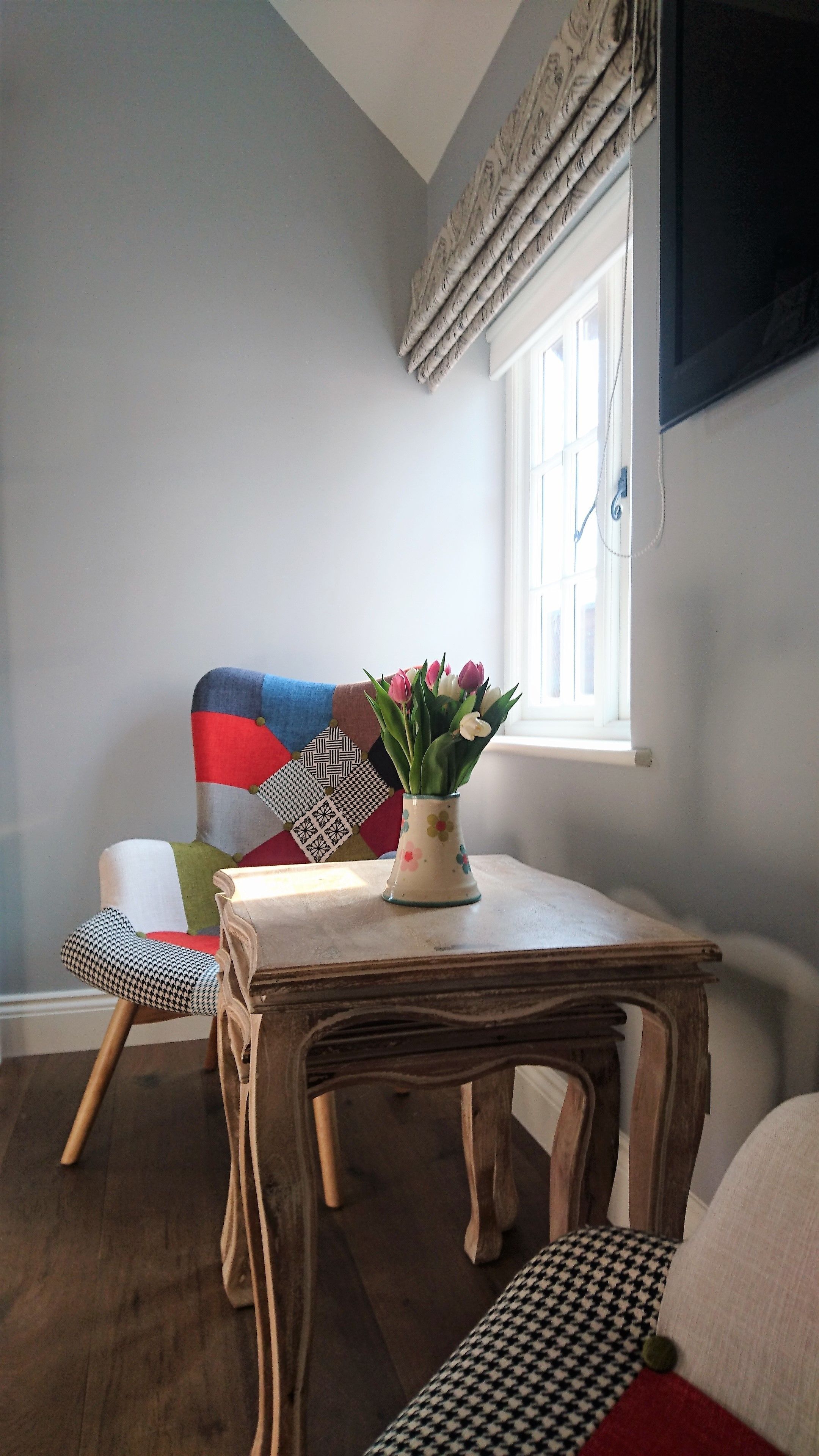 A dining area with a wooden table, a chair with a colorful cushion, and a vase with flowers.