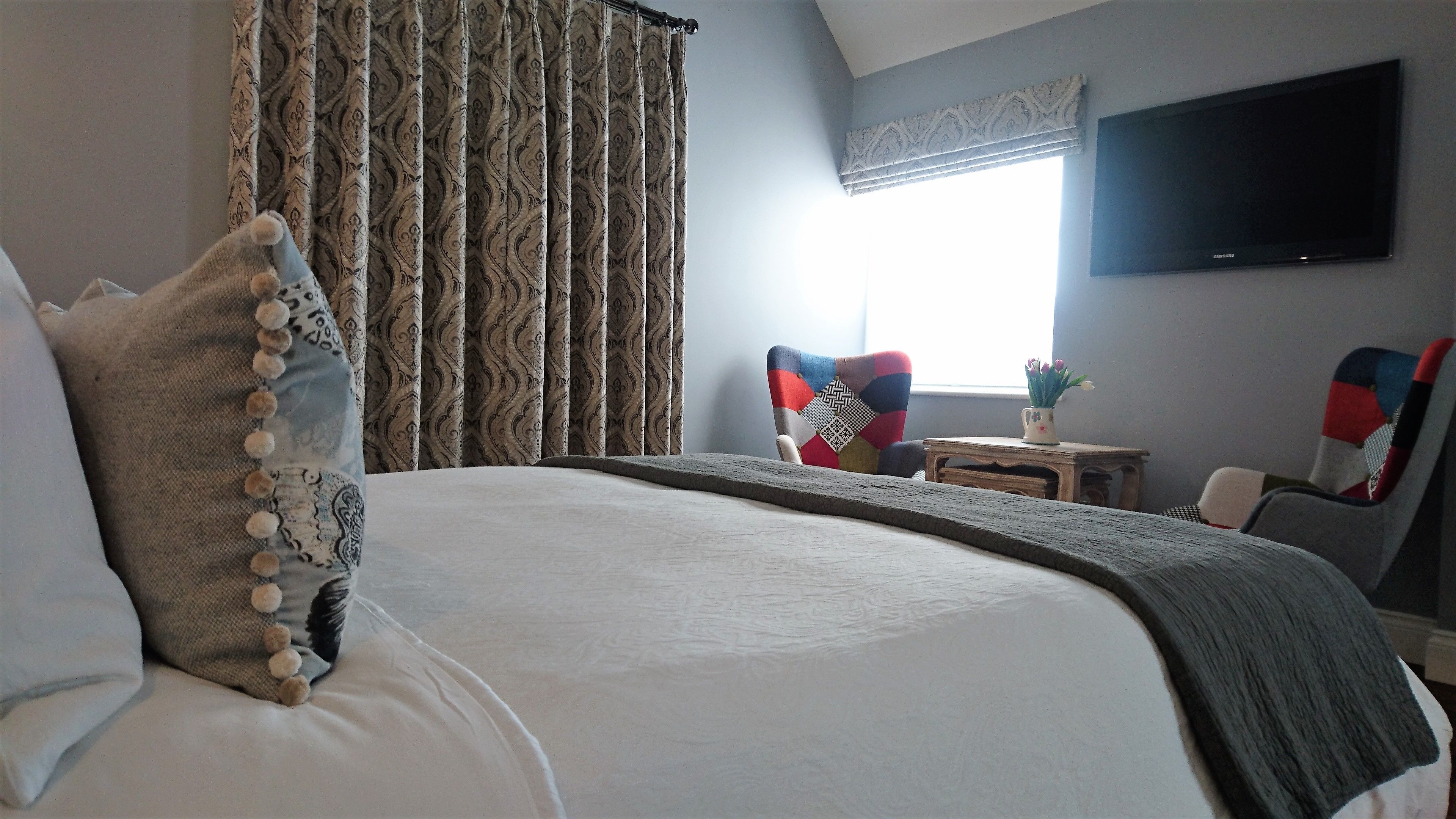 A bedroom with a large bed, a television on the wall, and a window with curtains.