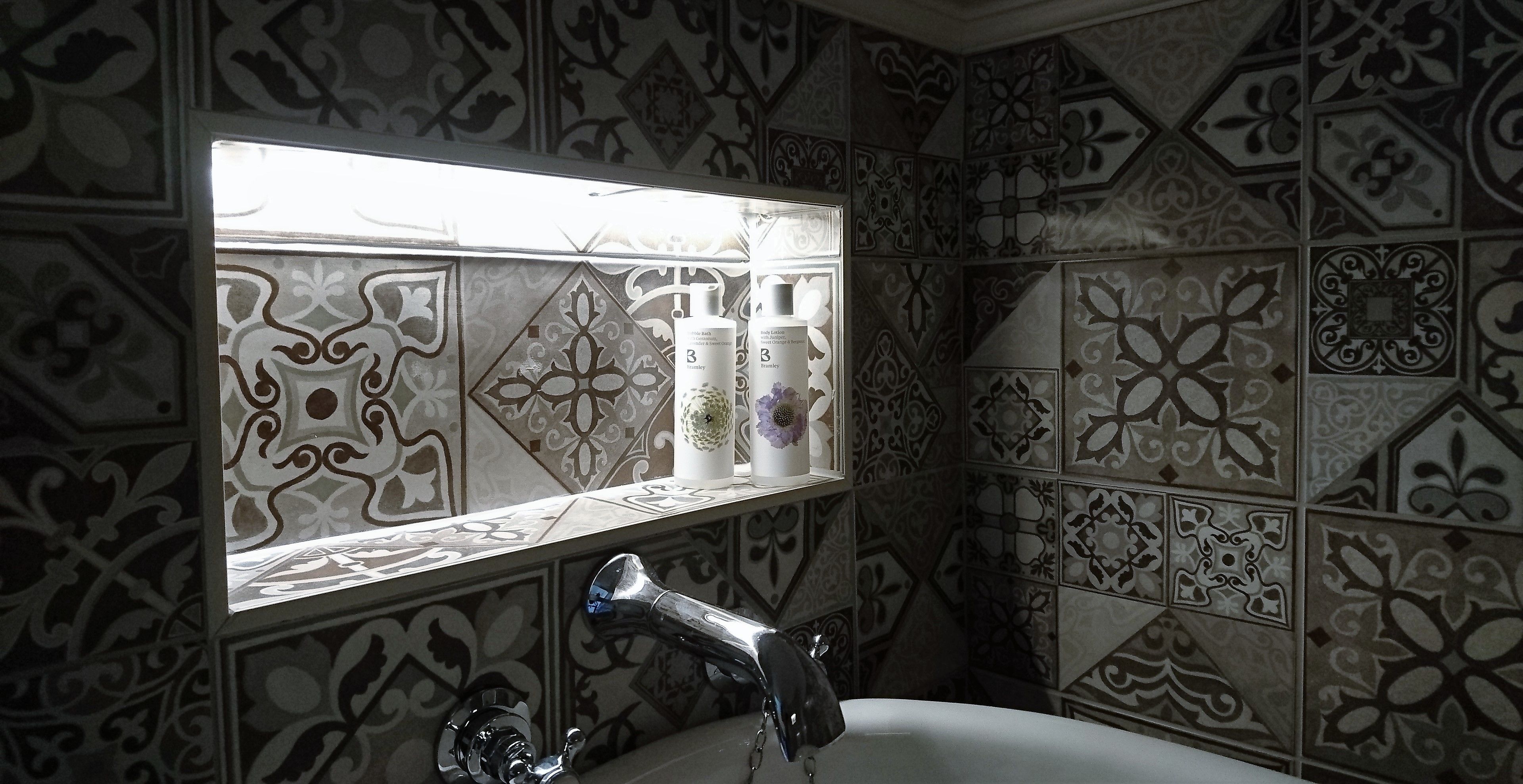 A bathroom with patterned tiles, a sink, and a window with bottles on the ledge.