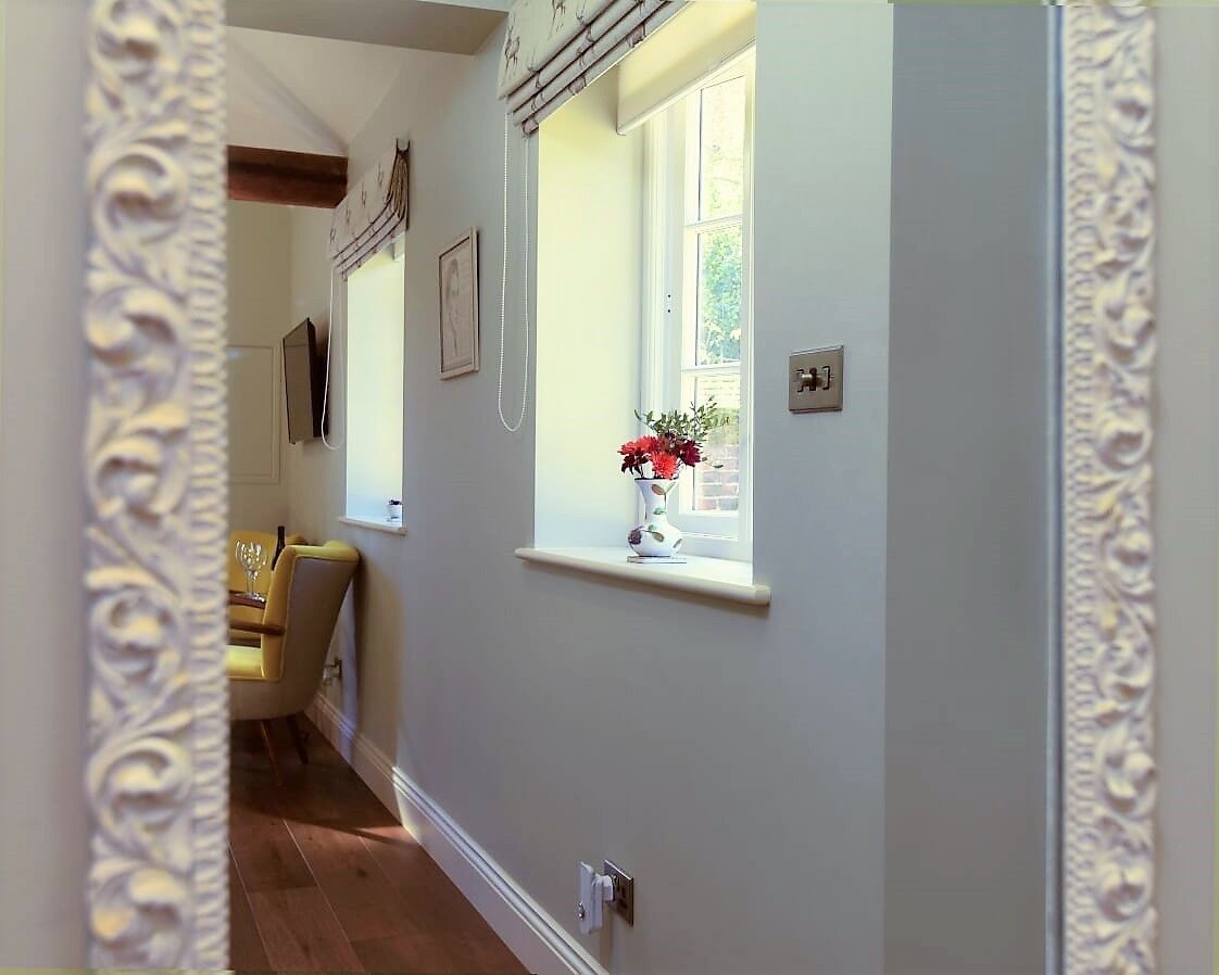 Un pasillo con una ventana, un florero con flores y una puerta con interruptor de luz.