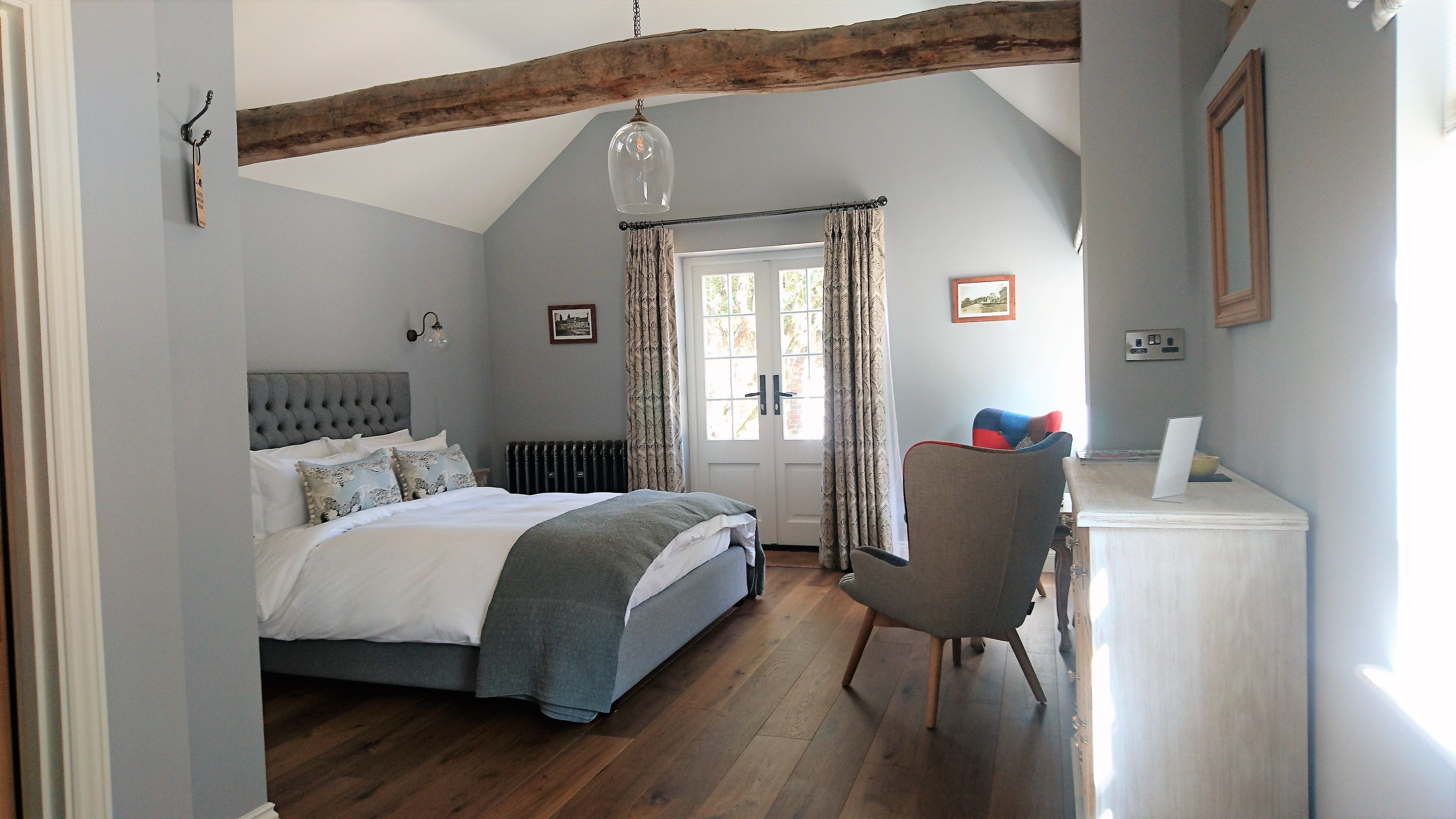 Een slaapkamer met een bed, een stoel, een bureau, een radiator en een raam met gordijnen.