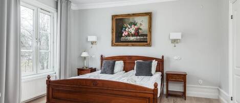 Un dormitorio con cama de madera, dos mesitas de noche, una lámpara de noche, una ventana con cortinas, un cuadro colgado en la pared y una alfombra roja.