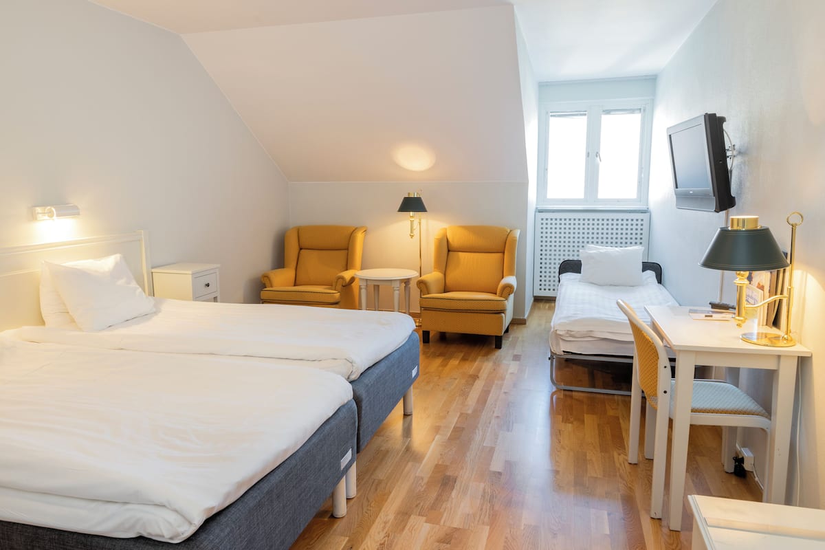 A hotel room with two beds, a desk, a chair, a TV, and a window.
