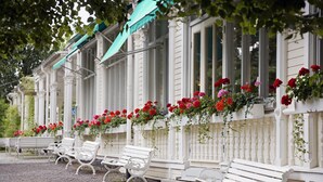 A row of white benches along a building with a green awning, and red flowers hanging from the windows. - Söderköpings Brunn (Soderkoping)