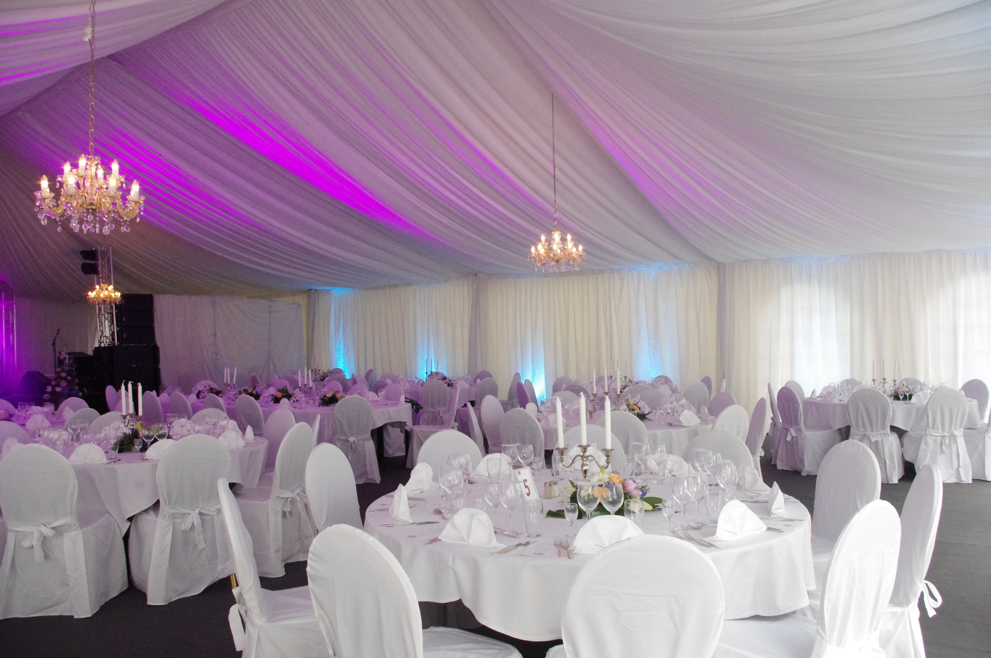 A banquet hall with round tables, white tablecloths, and chairs with white covers.