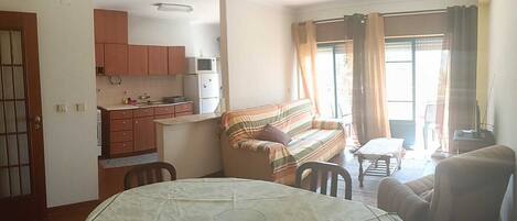 A compact living space with a dining table, sofa, kitchenette, and a view through a window.