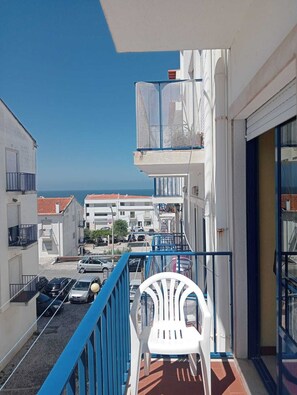 A balcony with a white plastic chair, a blue railing, and a view of the sea and buildings. - 2 bedroom apartment 5 minutes from the beach with sea views! (Nazaré)