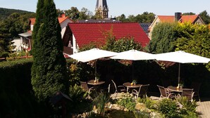 A garden with outdoor seating, a church steeple in the background, and a red-roofed building. - Hotel Garni Haus Sonneneck (Thale)