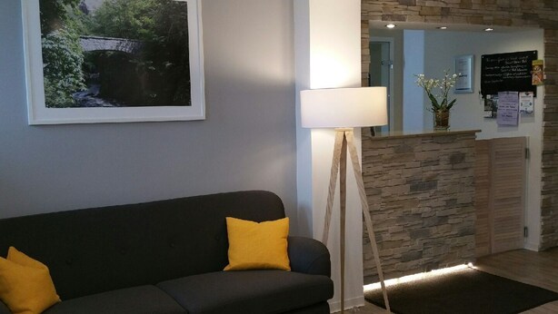 A modern reception area with a stone wall, a black sofa with yellow cushions, and a framed landscape photo on the wall. - Hotel Garni Haus Sonneneck (Thale)