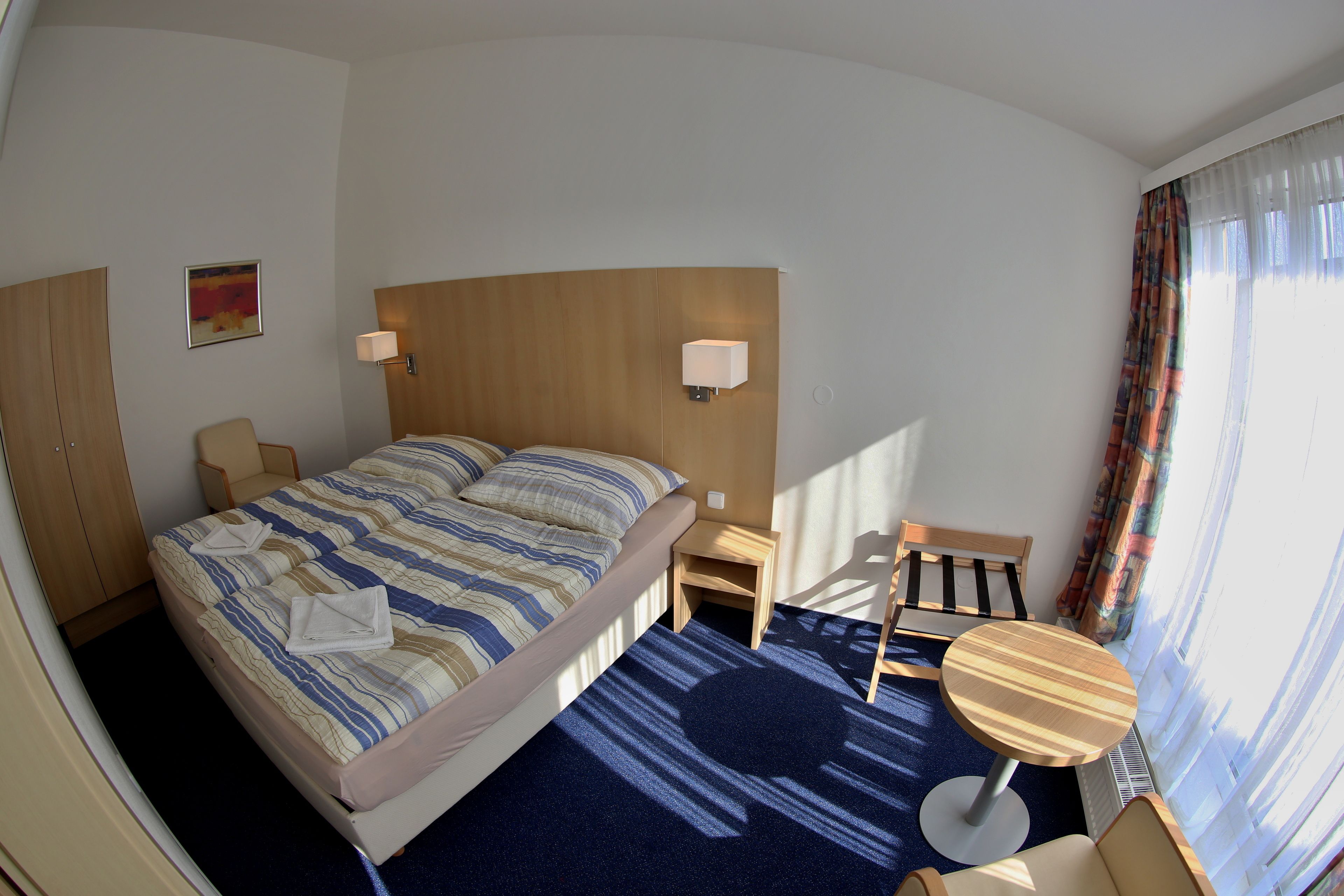 Une chambre d’hôtel avec un lit, un bureau, une chaise, une petite table et une fenêtre avec des rideaux.