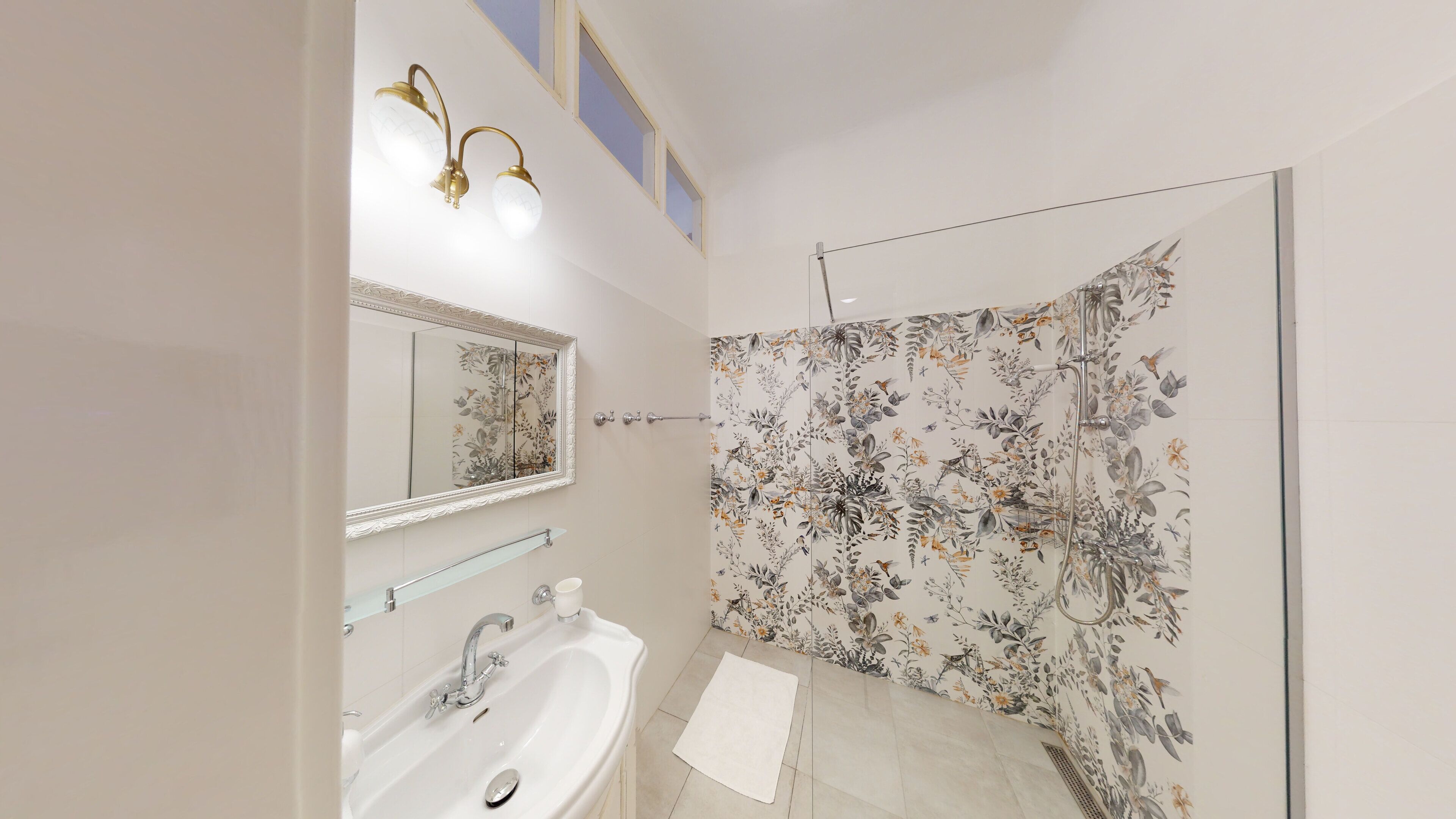 A bathroom with a white sink, a mirror, and a shower with floral wallpaper.