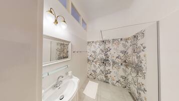 A bathroom with a white sink, a mirror, and a shower with floral wallpaper.