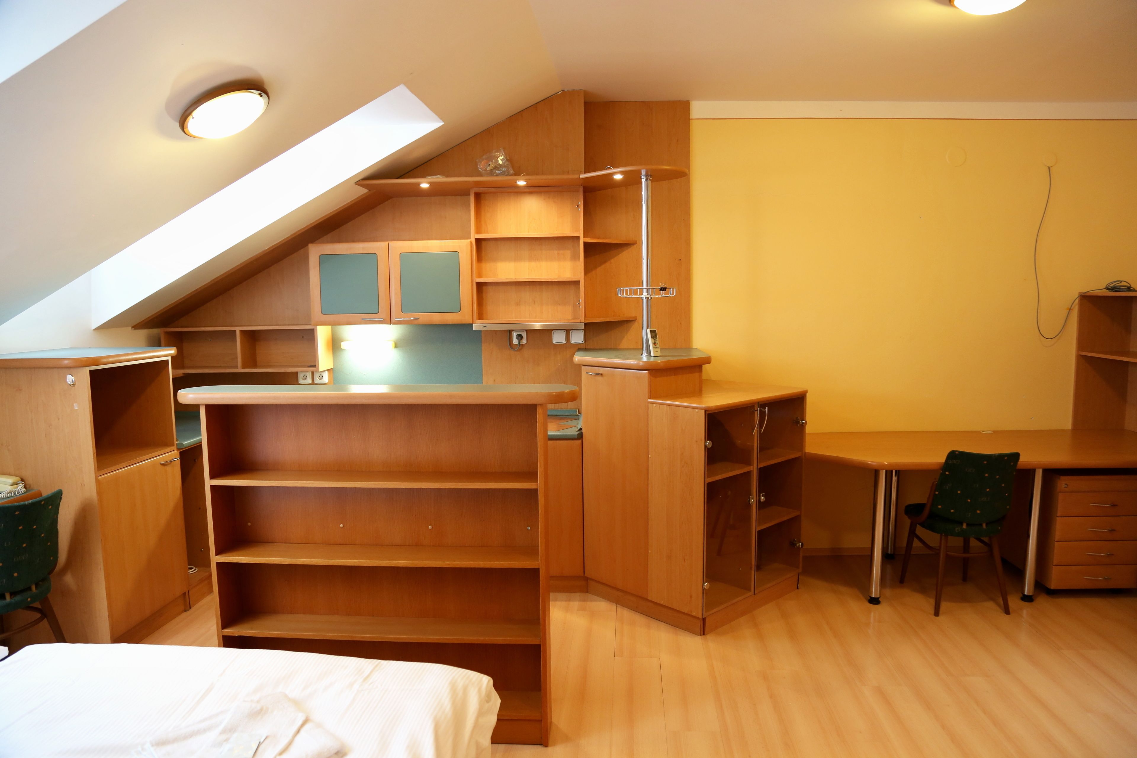 Ein kompakter, aufgeräumter Raum mit eingebauten Holzbögen, einem Schreibtisch und einem Stuhl, der durch eine geneigten Decke und ein Dachfenster gekennzeichnet ist.