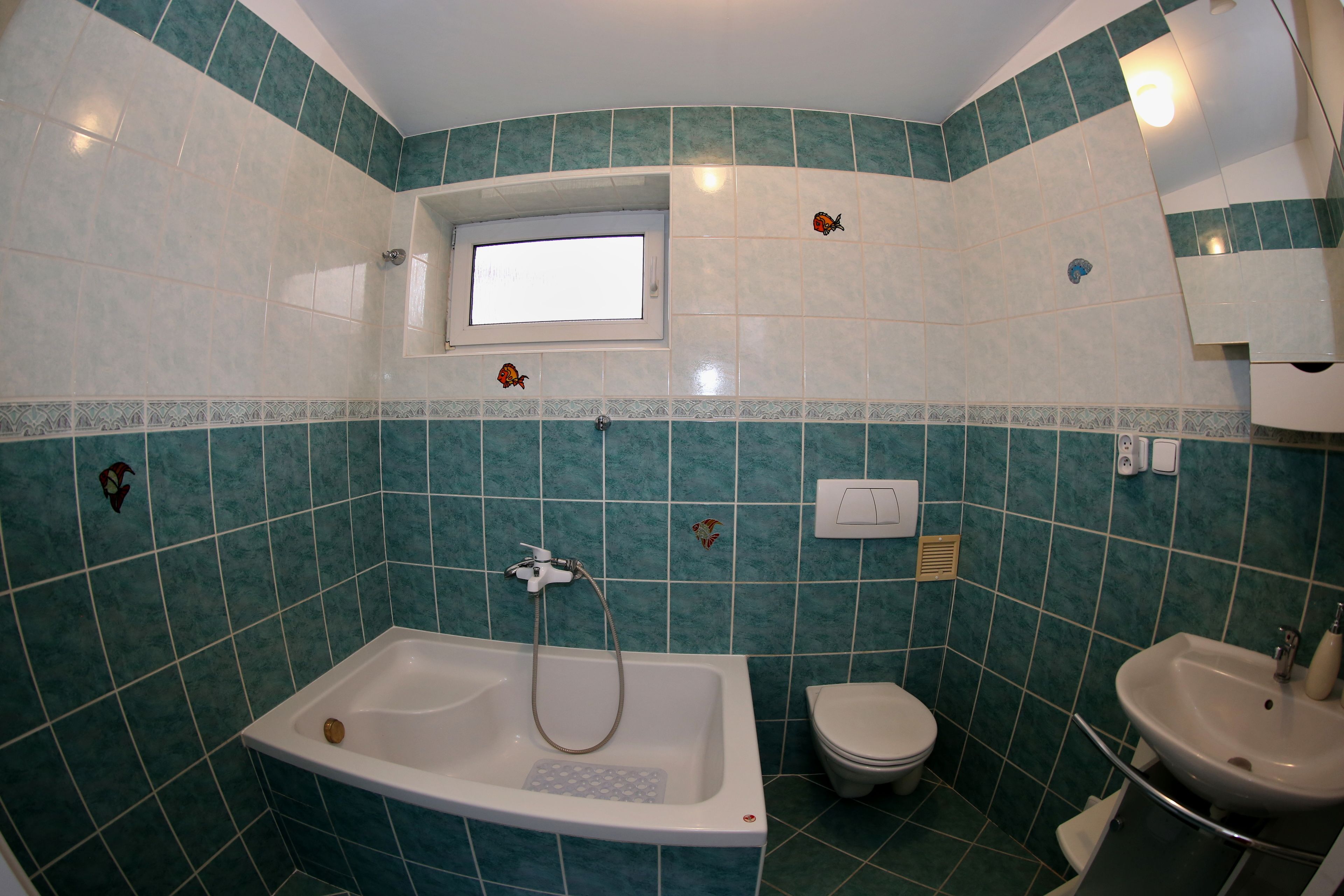 Un baño con bañera, inodoro y lavamanos, todo con azulejos verdes.