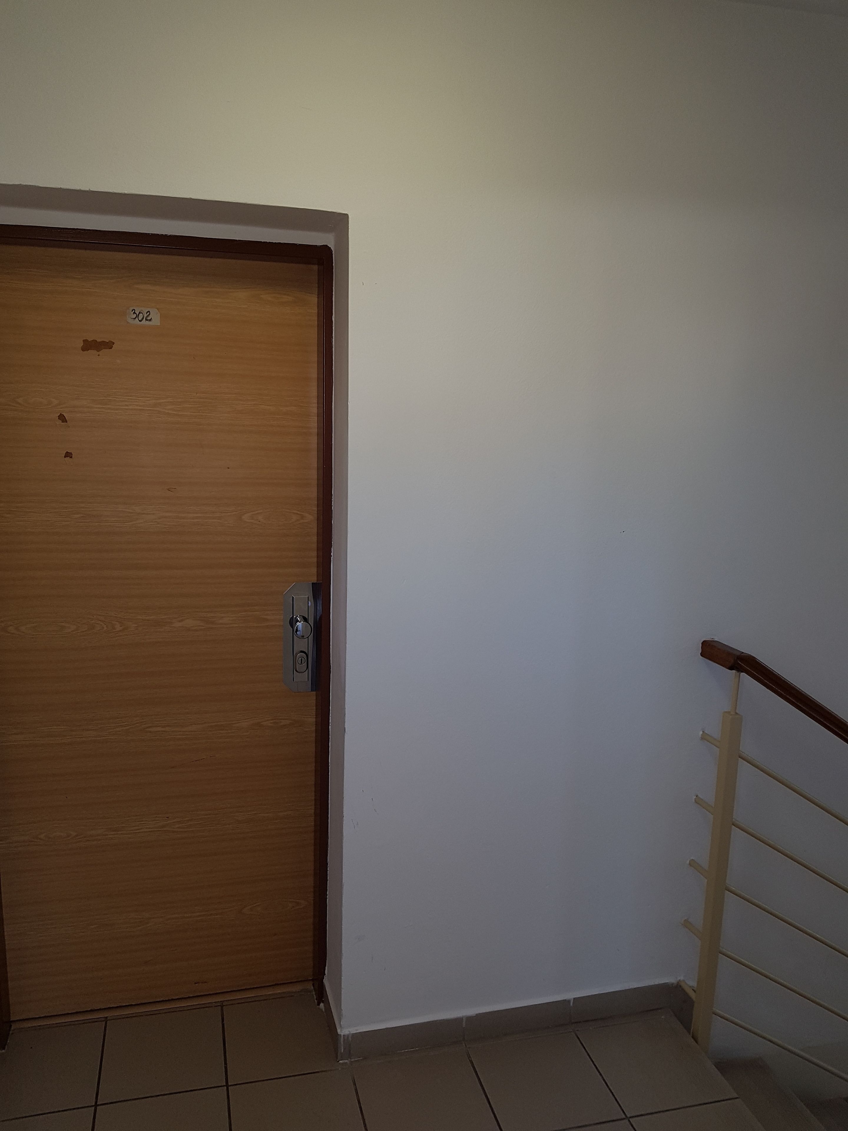Una porta in legno con una targa, una maniglia in metallo e un muro bianco con una ringhiera in legno.