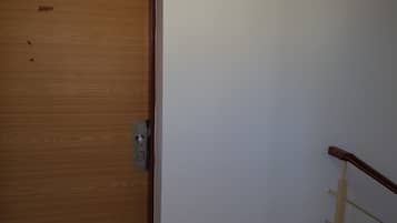 A wooden door with a number plate, a metal handle, and a white wall with a wooden handrail.