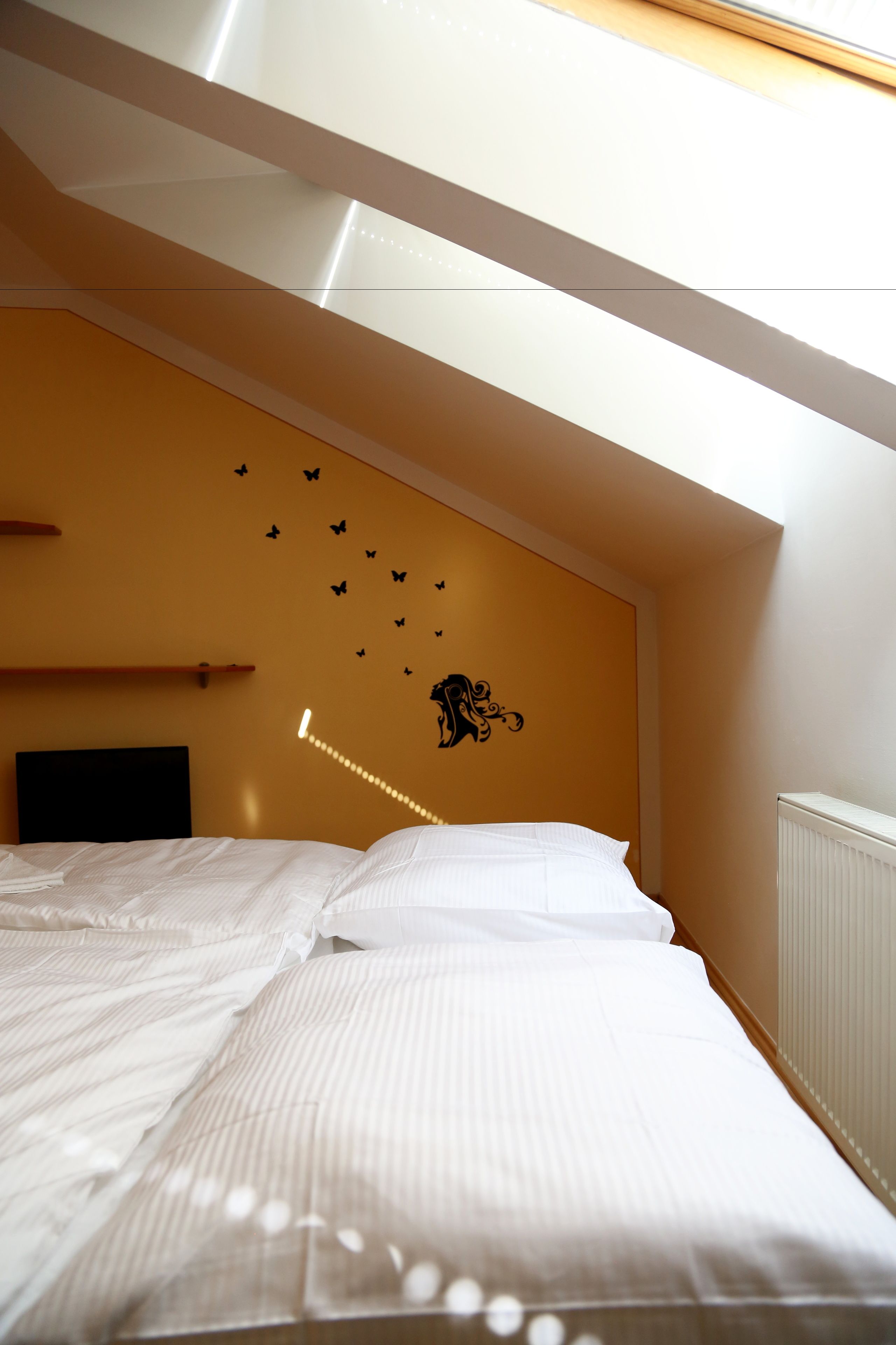 A bedroom with a sloped ceiling, a bed with white linens, a wall-mounted shelf, and butterfly decals.