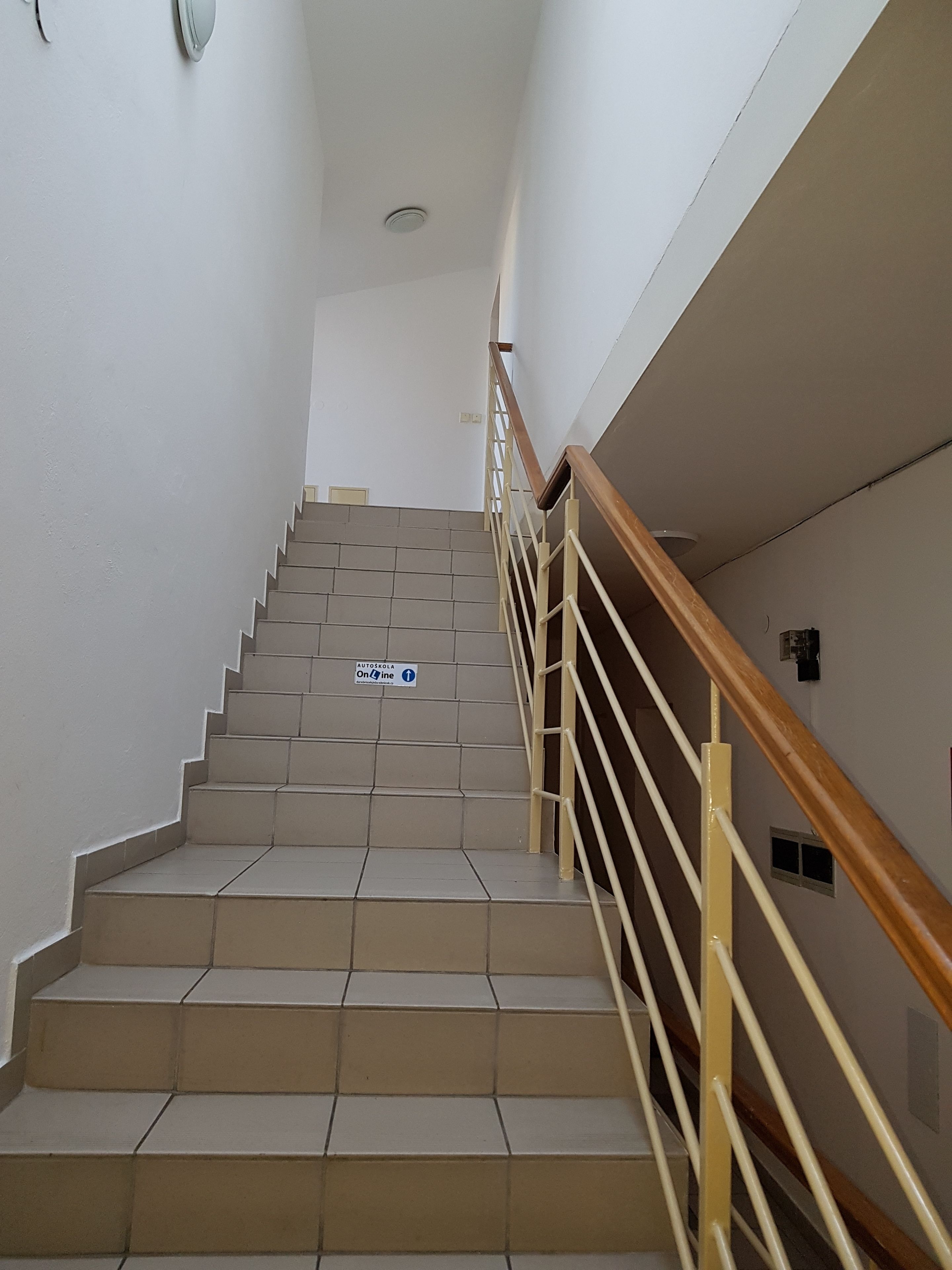 A staircase with beige tiles and a wooden handrail, leading to an upper floor.