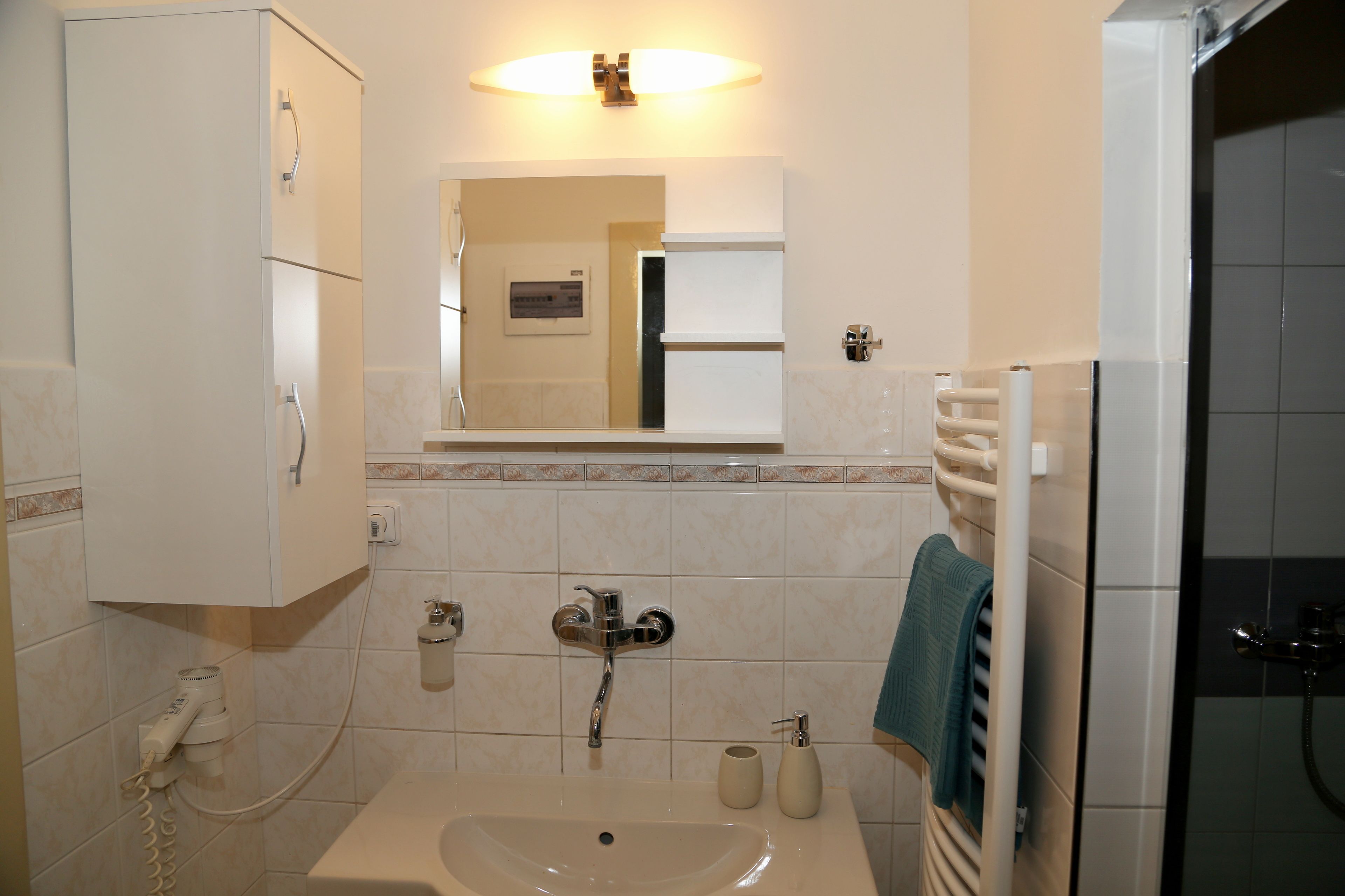 A bathroom with a sink, mirror, towel rack, and a shower area.