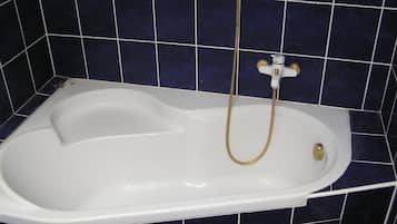 A bathtub with a handheld showerhead in a room with dark blue tiled walls.