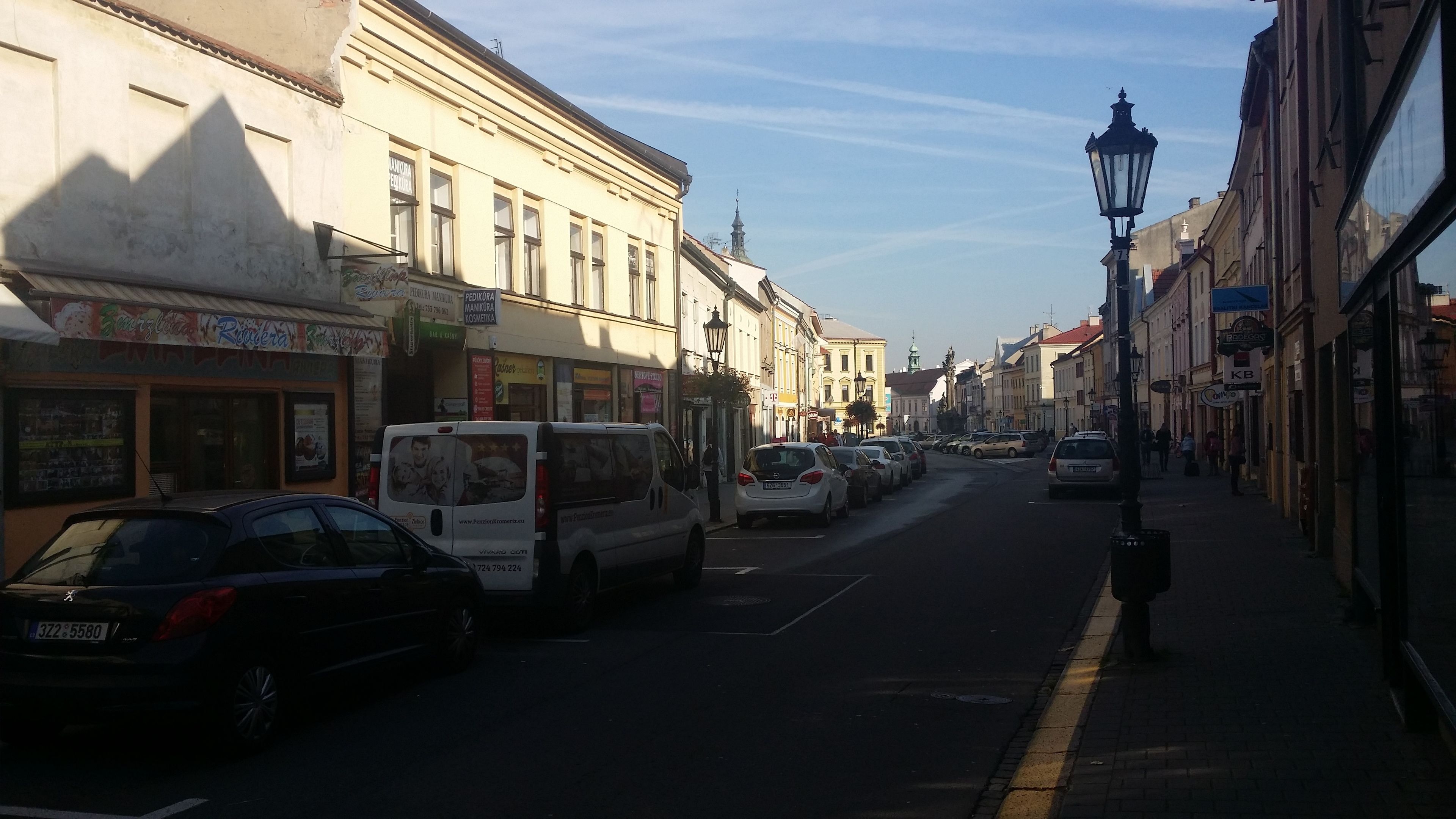 A street lined with buildings, some with signage, parked cars, and a clear sky.