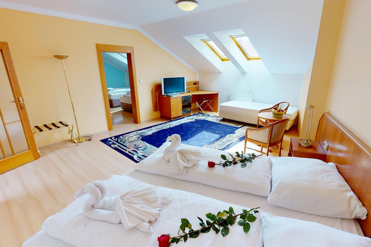 A hotel room with two beds, a desk, a chair, a small table, and a TV.