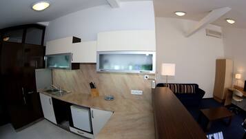 A compact kitchen with a microwave, sink, and small refrigerator. There is a flat-screen TV mounted above the counter. A sofa and a small table are in the living area.