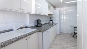 A modern kitchen with white cabinetry, a granite countertop, a sink, a coffee maker, and a refrigerator. - Ocean view condo located in front of the beach with sunny terrace - only families (Playa de Gandía)