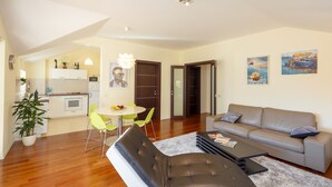 A modern living room with a sofa, coffee table, and dining area. There is a kitchen in the background with white cabinets and a dining table. - New brand apartment with sea view  (Dubrovnik)