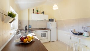 A modern kitchen with white cabinets, a microwave, a refrigerator, a sink, and a countertop with a fruit bowl. - New brand apartment with sea view  (Dubrovnik)