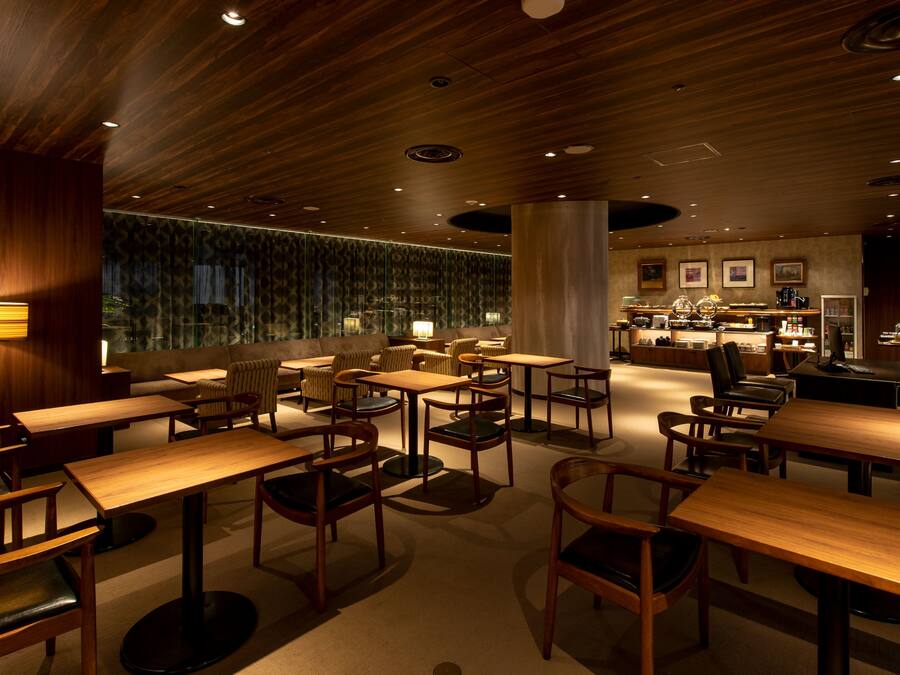 A modern restaurant with wooden tables and chairs, a bar area, and a view of the cityscape.