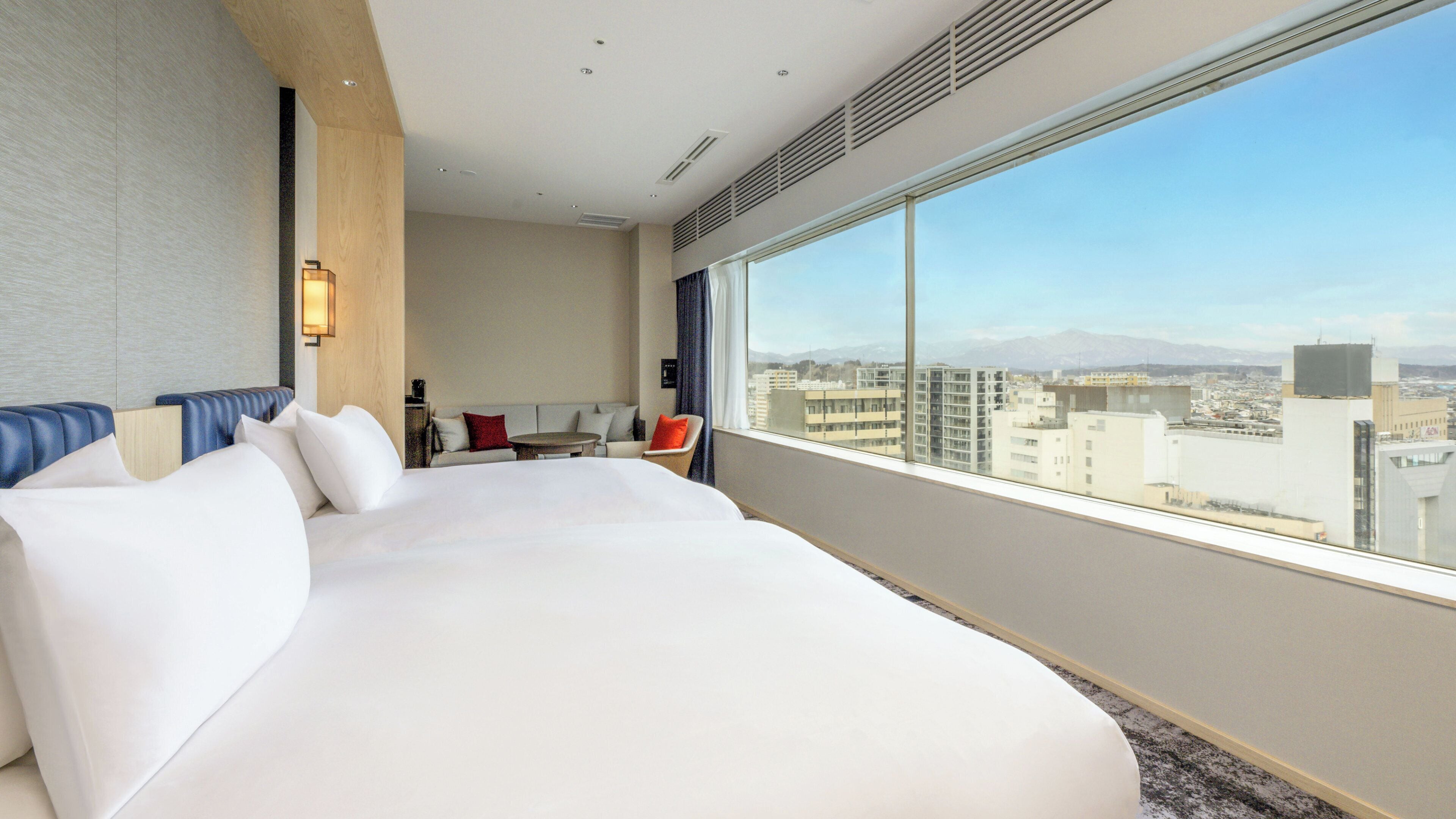 A hotel room with a large bed, a seating area with a table and chairs, and a large window offering a city view.