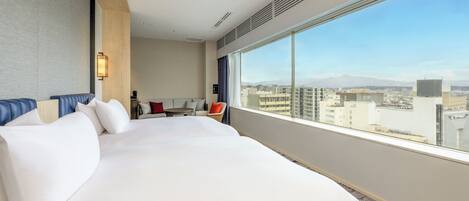 Ein Hotelzimmer mit einem großen Bett, einer Sitzecke mit Tisch und Stühlen sowie einem großen Fenster mit Blick auf die Stadt.
