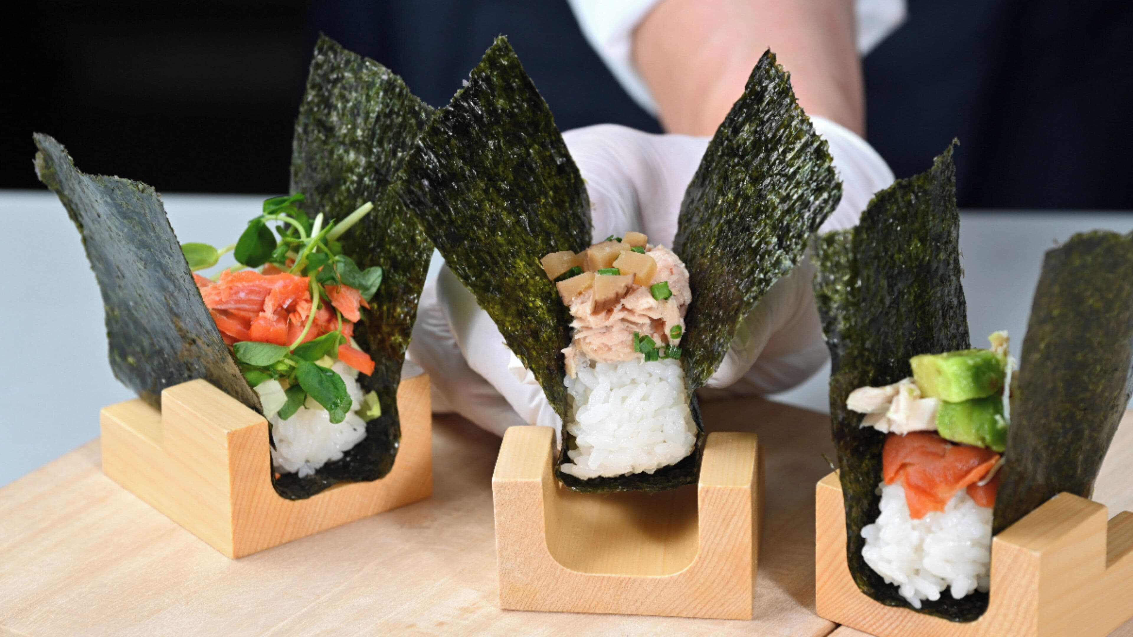 Three sushi rolls on wooden stands.