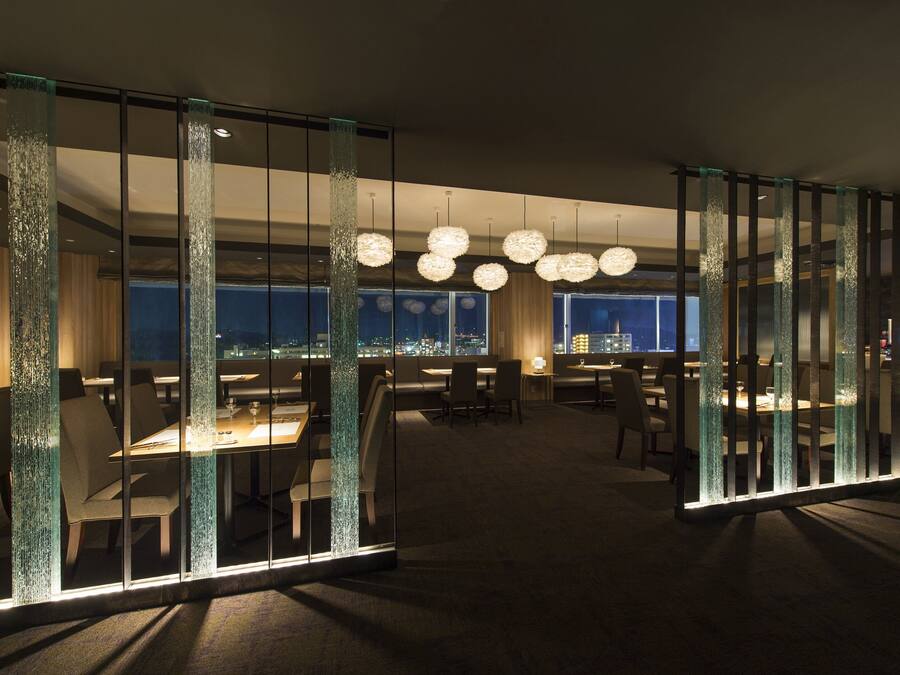 A modern hotel lobby with glass partitions, round chandeliers, and a city view.
