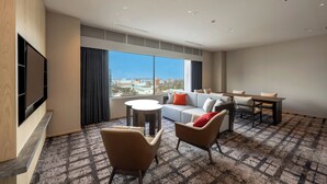A modern hotel room with a large window, a sofa, two armchairs, a small round table, and a TV mounted on the wall. - ANA Crowne Plaza Akita by IHG (Akita)
