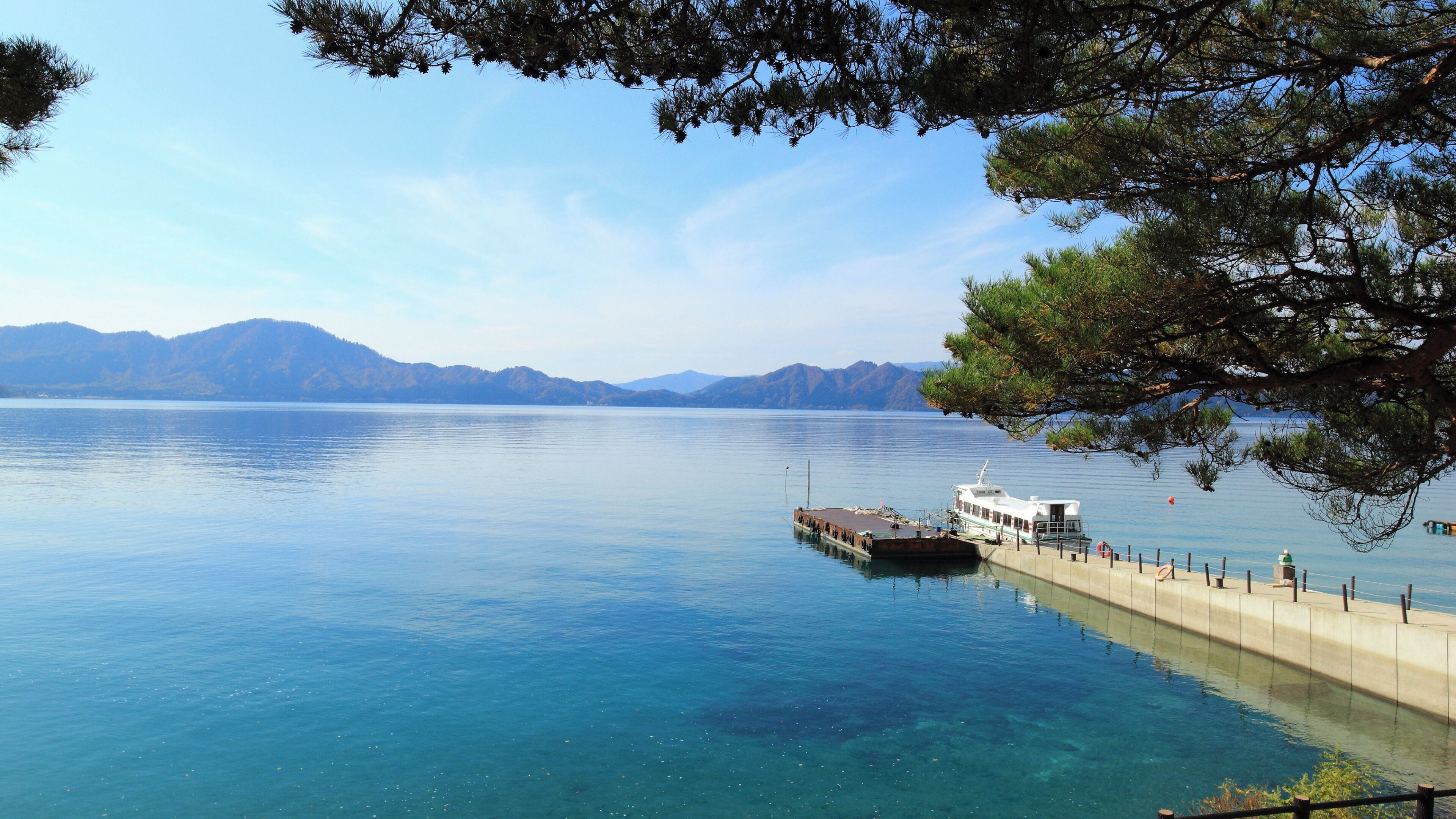 A calm lake with a dock and a boat, surrounded by mountains and clear skies.