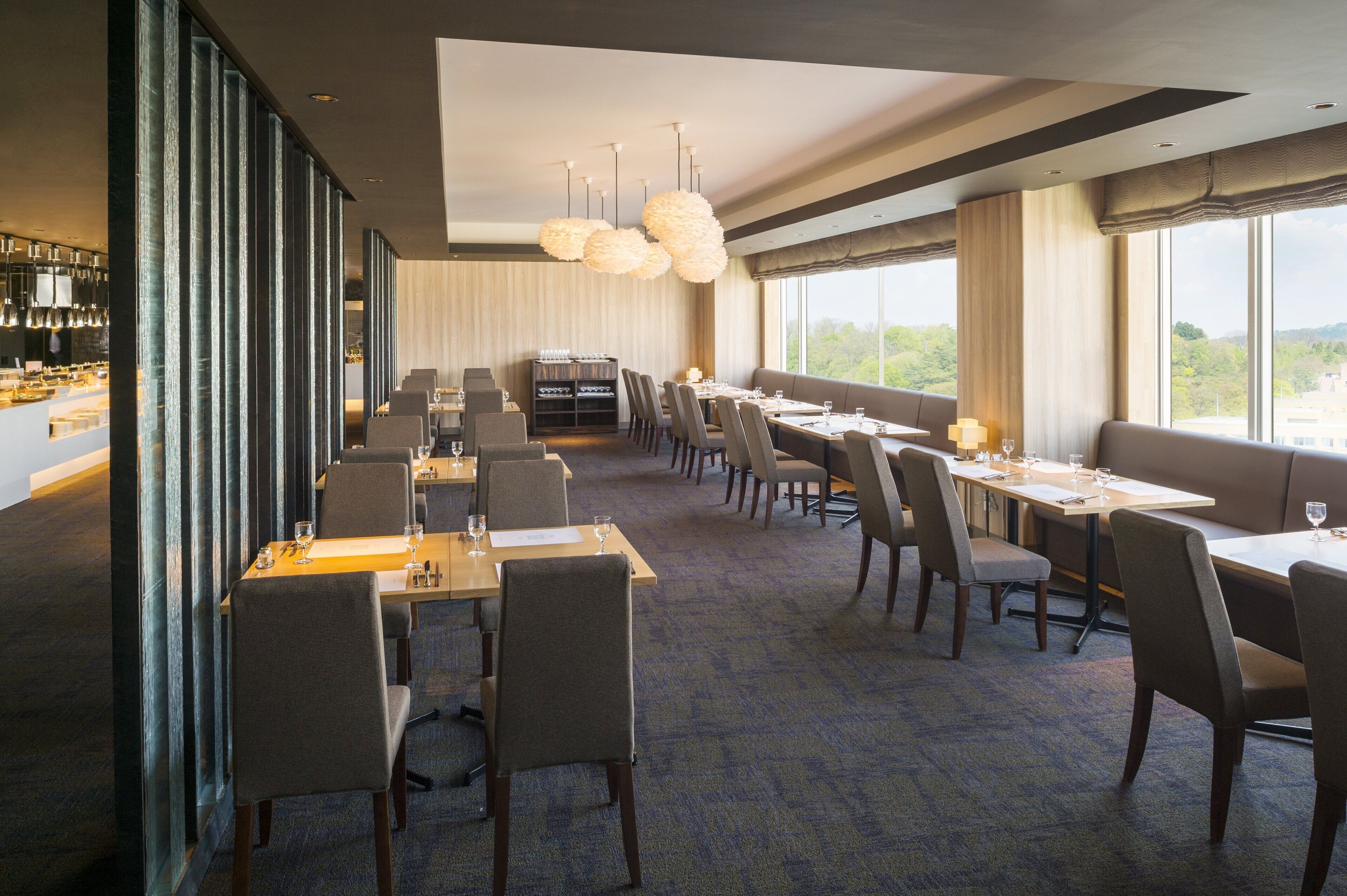 En restaurant med flere spiseborde og stole, et barområde og store vinduer med udsigt over det fri.