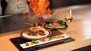 A dining table with a lobster dish, a glass of white wine, and a plate of vegetables.