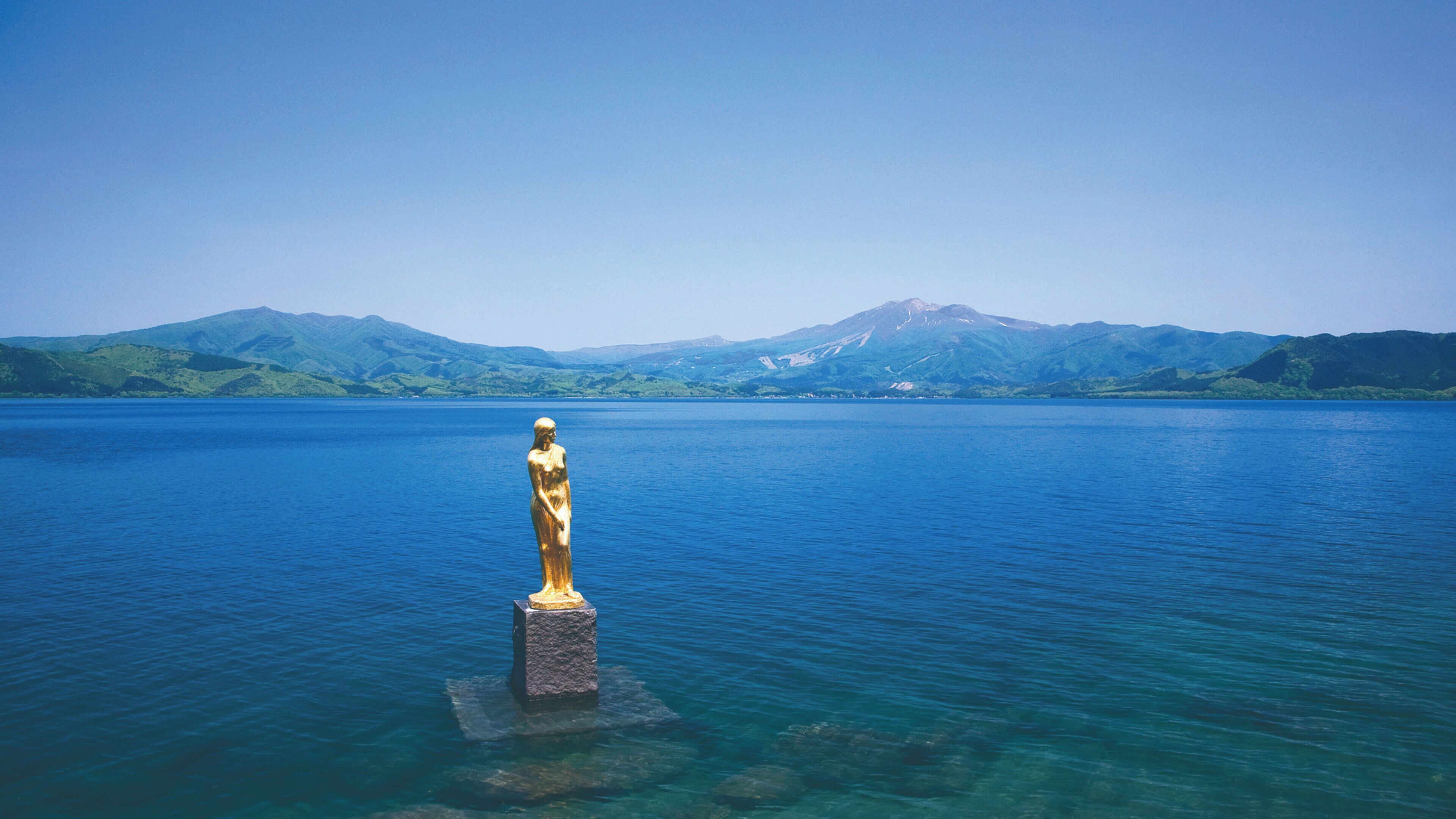 A statue in a body of water with mountains in the background.