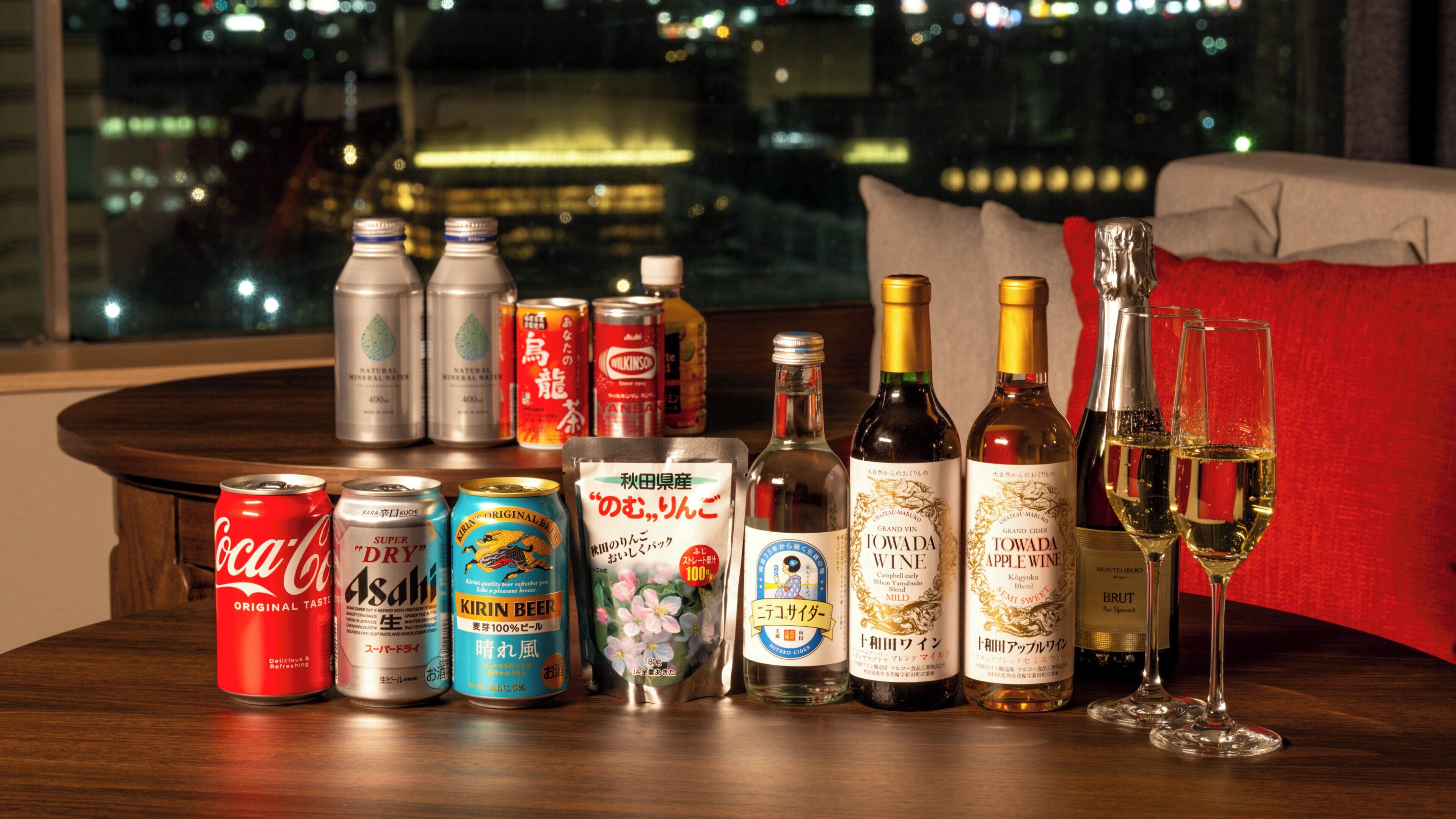 Une variété de boissons, notamment du Coca-Cola, de la bière Kirin et du vin, sont disposées sur une table, avec une vue sur la ville en arrière-plan.