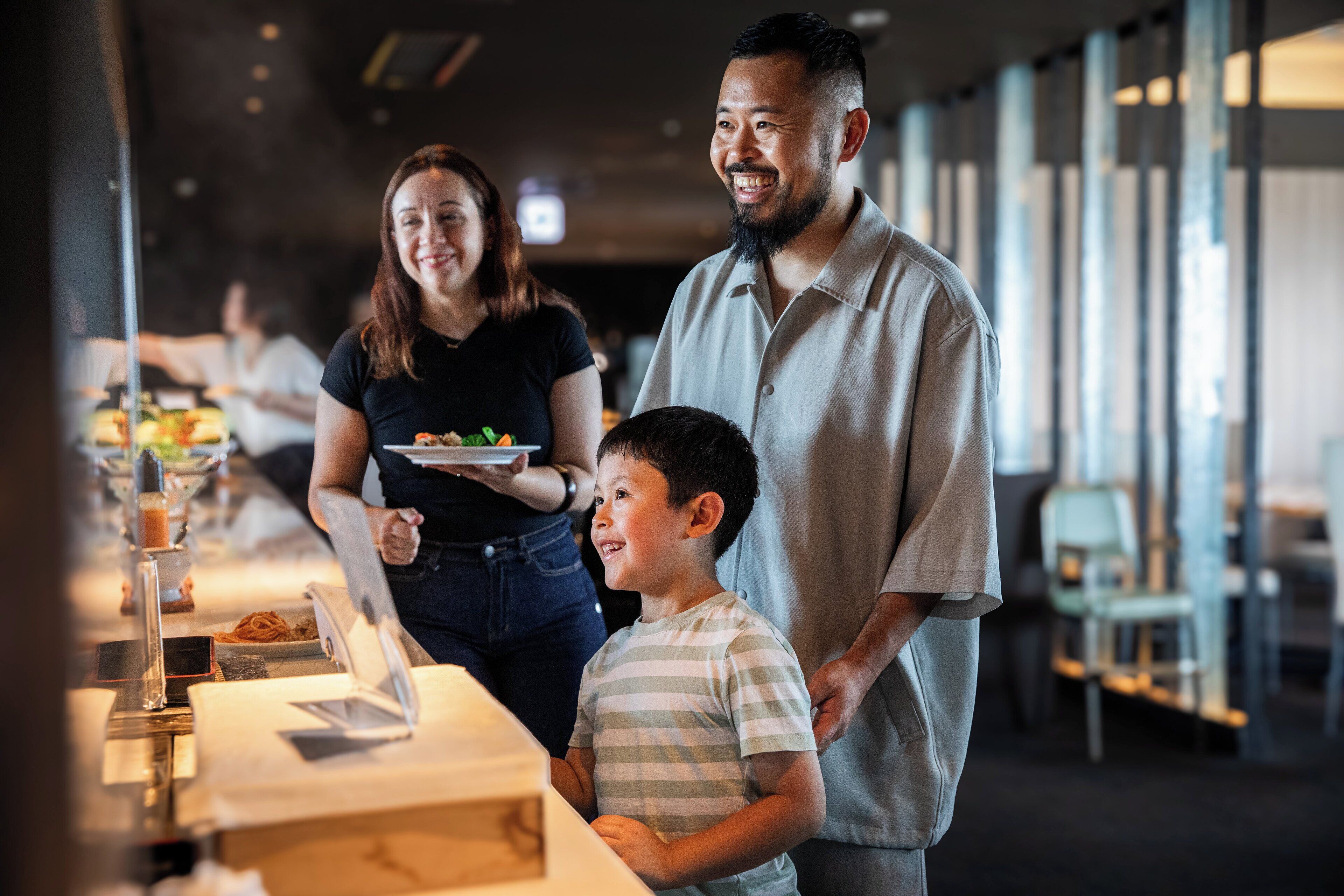 Una família dinueig en un restaurant modern amb un taulell llarg i una varietat de plats.