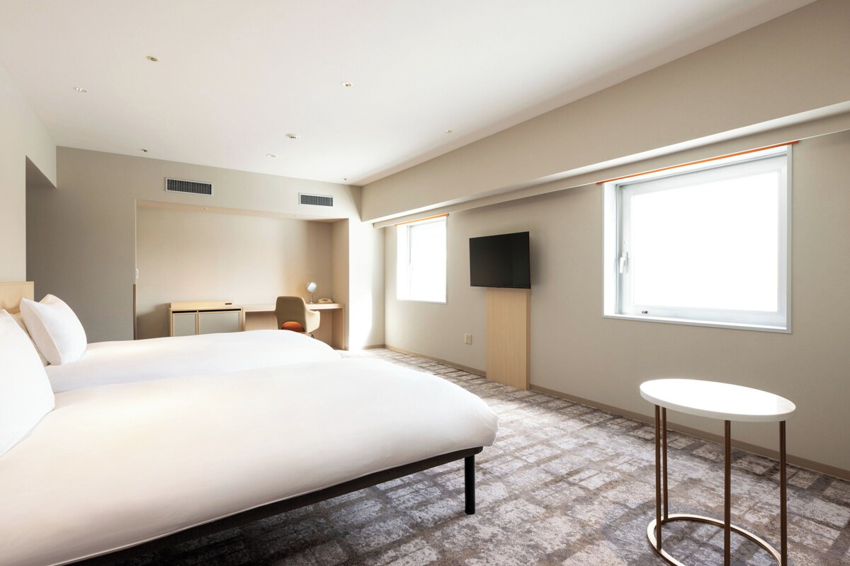A hotel room with a large bed, a desk, a chair, a TV, and a small table.