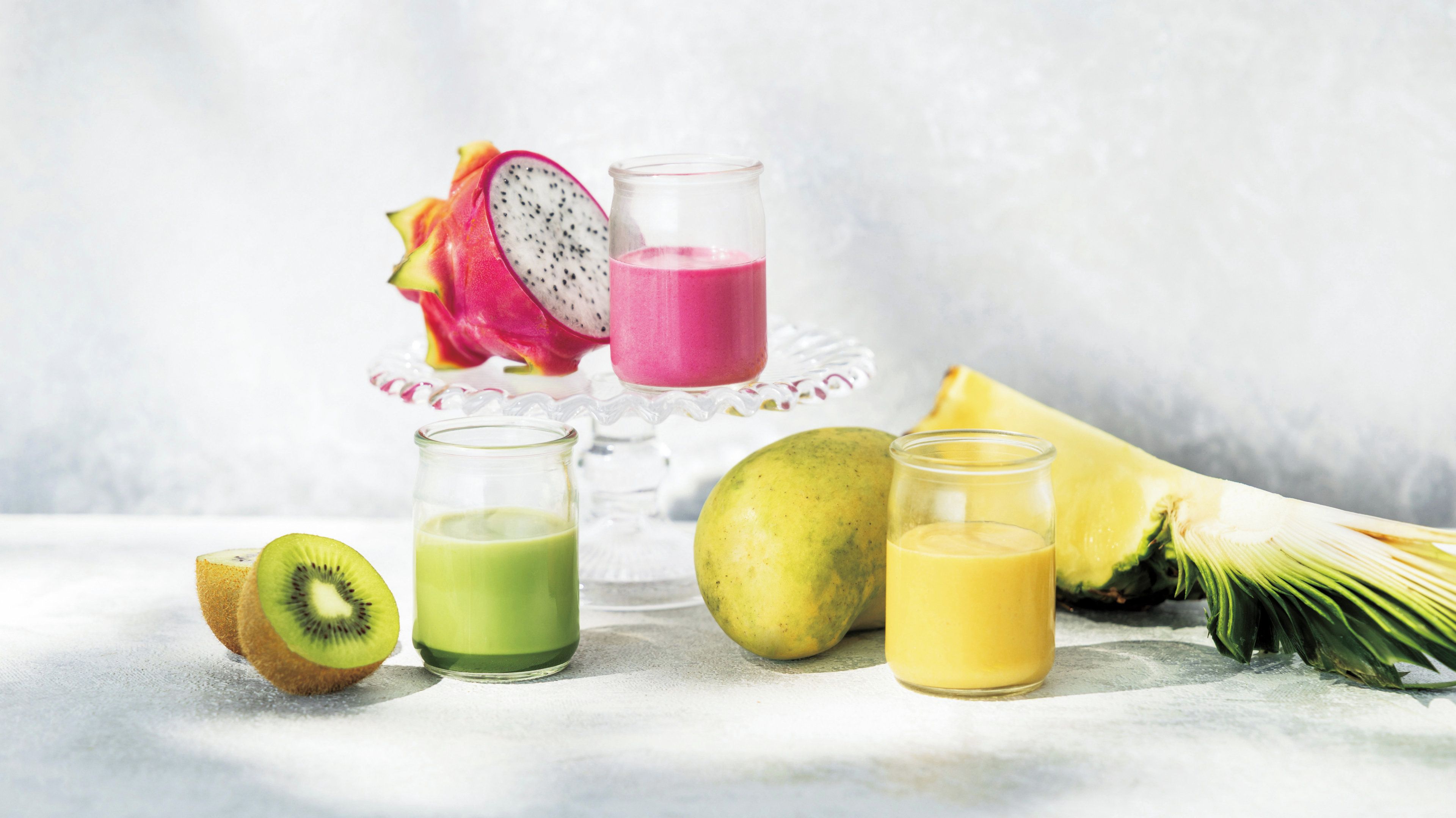 Una variedad de frutas y jugos, como pitaya, kiwi y piña, dispuestas sobre una superficie de mármol.