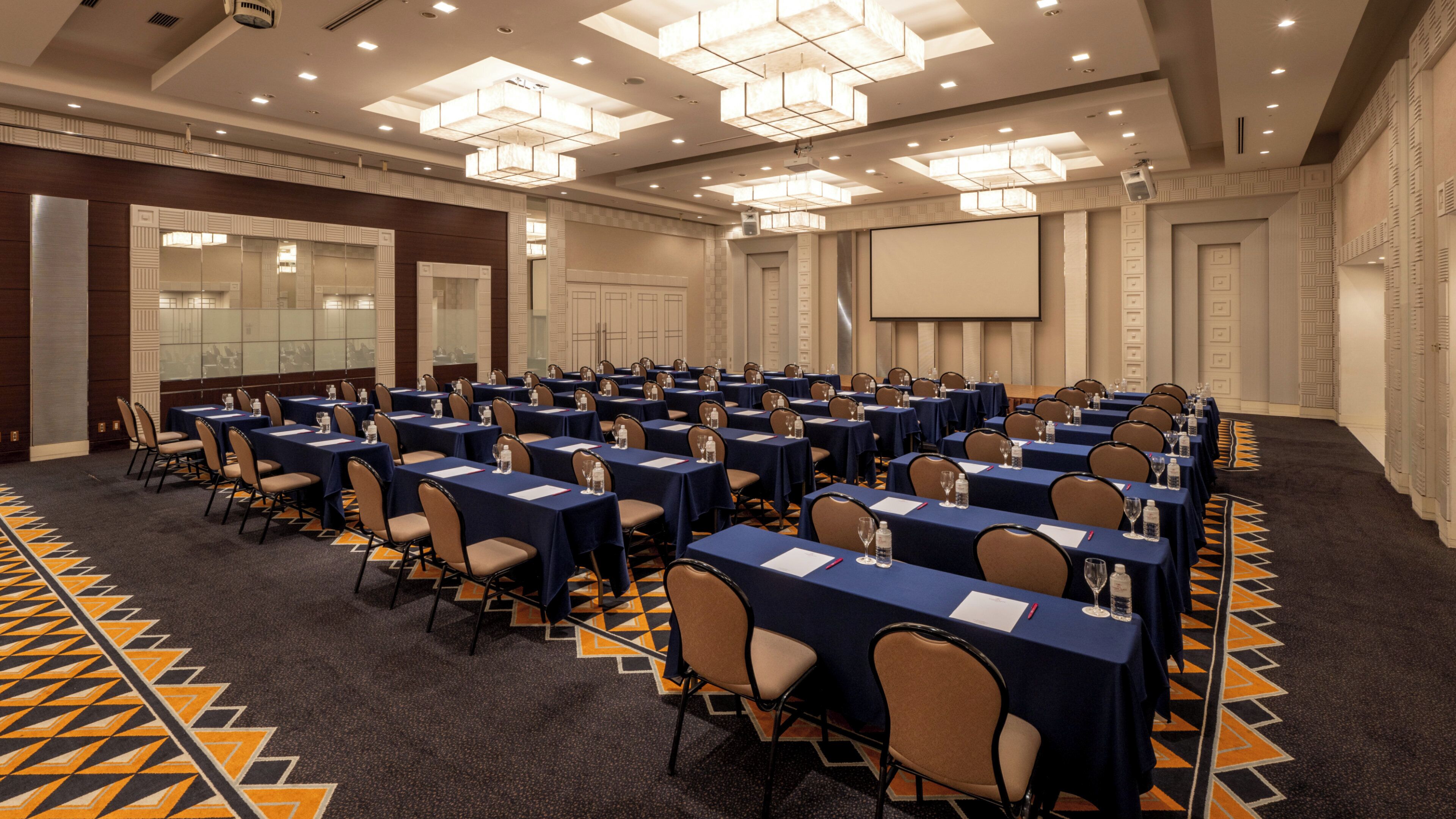 A conference room with multiple tables and chairs, a large screen, and a patterned carpet.