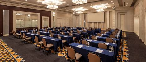 A conference room with multiple tables and chairs, a large screen, and a patterned carpet.