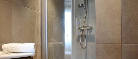 Un baño moderno con ducha envuelta en vidrio, tocador de madera y azulejos color crema.