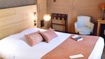A hotel room with a large bed, a chair, a desk, and a wall-mounted light fixture.