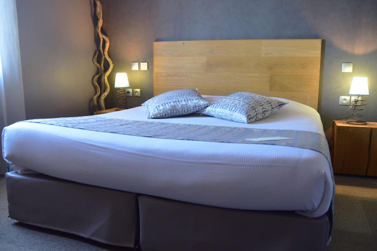 Een groot bed met een houten hoofdeinde, twee bedlampjes en een decoratief wandobject.